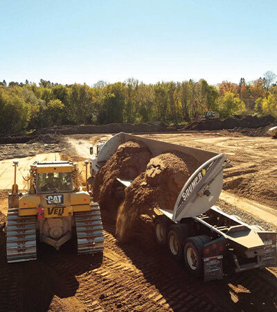 Bulldozer loads dirt into dump truck at construction site.