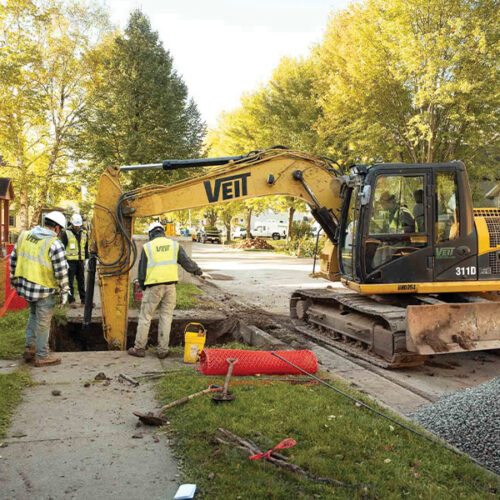 Workers use an excavator to dig a trench on a street.