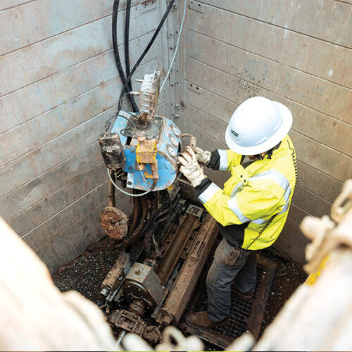 Worker in hard hat operates machinery in excavated pit.
