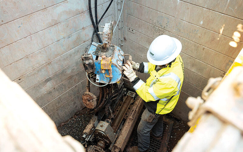 Worker in hard hat operates machinery in excavated pit.