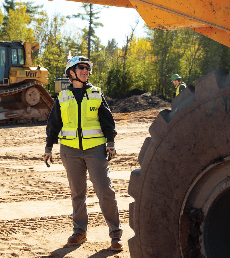 Construction worker in helmet and vest by machinery at worksite.