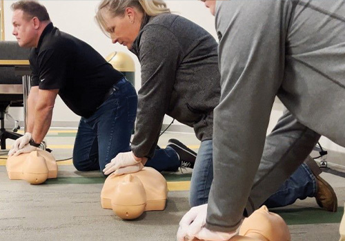Three people kneeling, practicing CPR on training manikins.