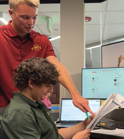 Two young men review papers in an office together.
