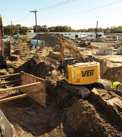 Yellow VENT excavator moves dirt at busy construction site.