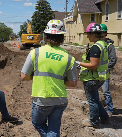 Three construction workers at a dirt worksite with excavator.
