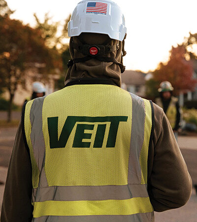Worker in white hard hat and VEIT vest outdoors.