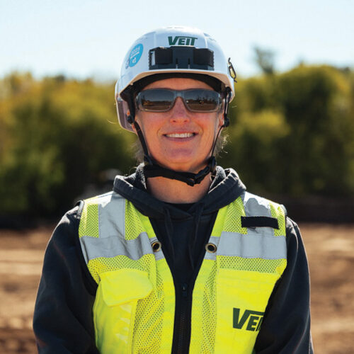 Person in hard hat and vest at outdoor construction site.