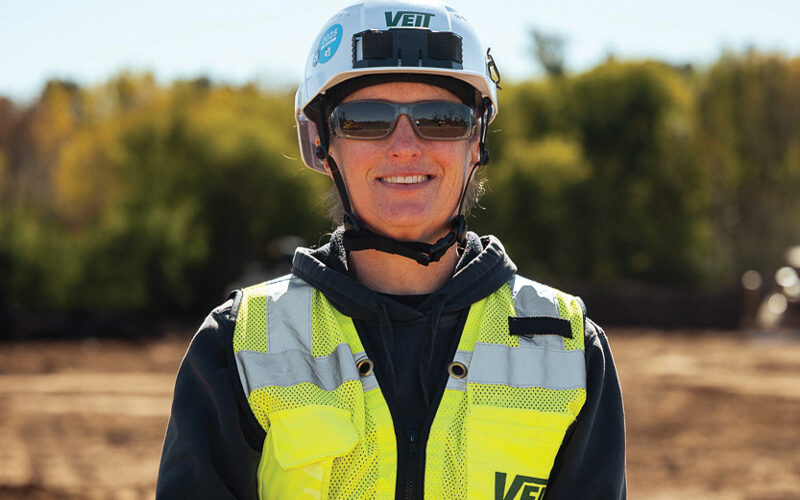 Person in hard hat and vest at outdoor construction site.