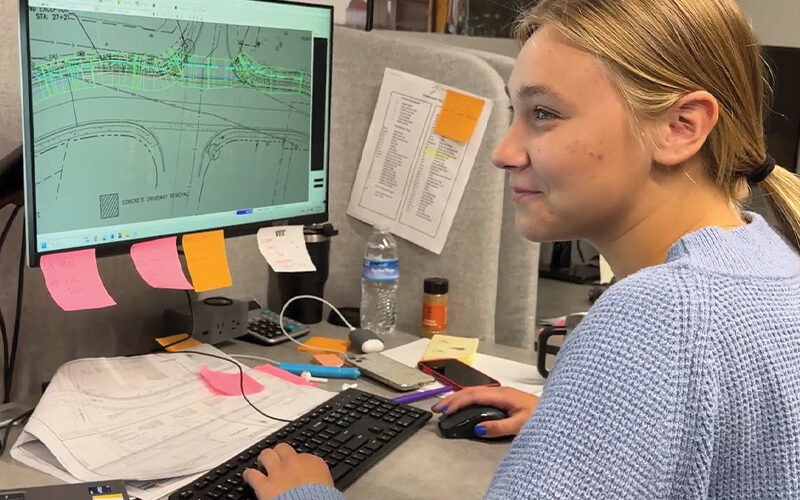 Woman at desk works on plans, surrounded by office items.