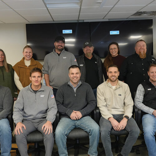 Eleven adults pose together in an office with monitors.