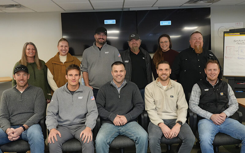 Eleven adults pose together in an office with monitors.