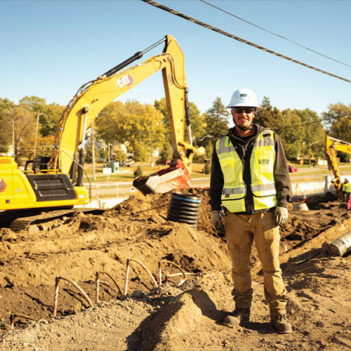 Construction worker in hard hat at site with excavators.